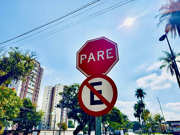 Placa com a indicação "Pare" e "Proibido estacionar", com um prédio ao fundo.